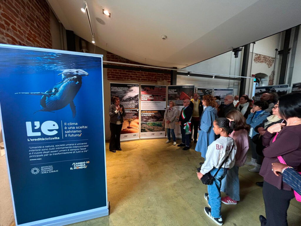 Visitatori ascoltano una guida che presenta i pannelli della mostra “L’eredità della vita” a Marcallo con Casone.