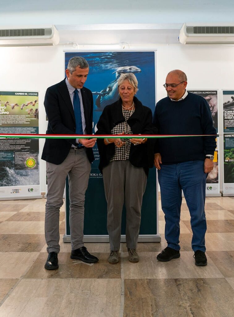 Tre persone tagliano un nastro tricolore durante l’inaugurazione della mostra “L’eredità della vita” a Guidonia Montecelio.