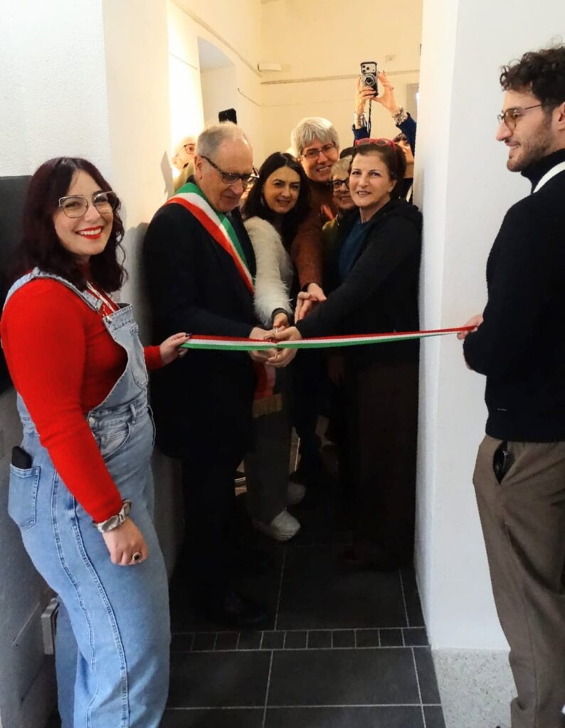 Cerimonia di inaugurazione con il sindaco che taglia il nastro tricolore, circondato da cittadini in uno spazio espositivo.