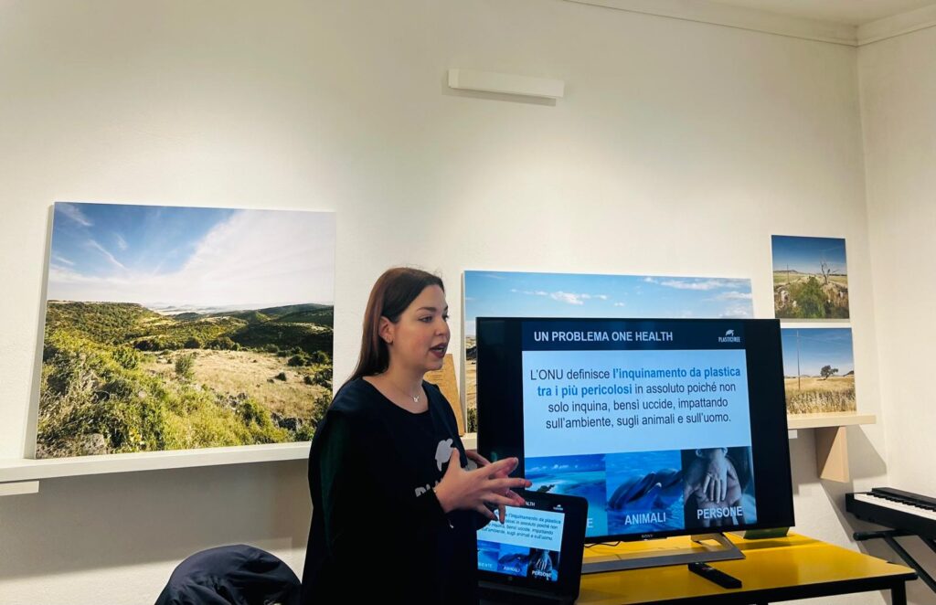 Relatrice presenta un intervento sull’inquinamento da plastica davanti a uno schermo con slide informative in una sala espositiva.