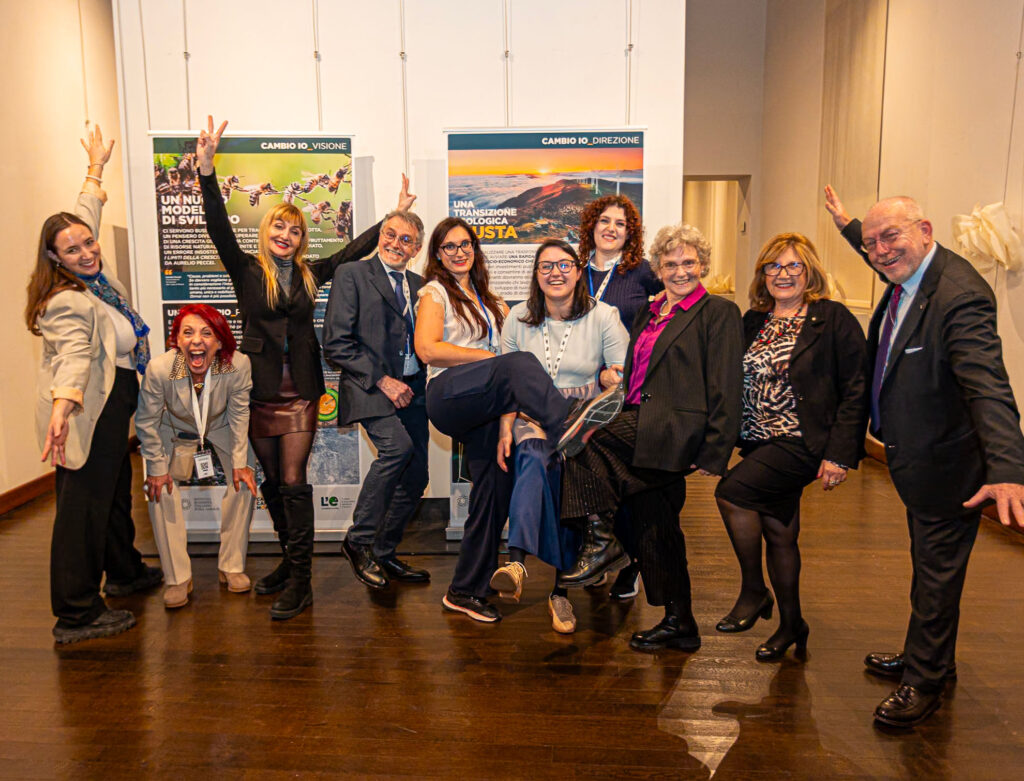 Parte del gruppo dell’inaugurazione posa in modo informale e sorridente davanti ai pannelli espositivi.