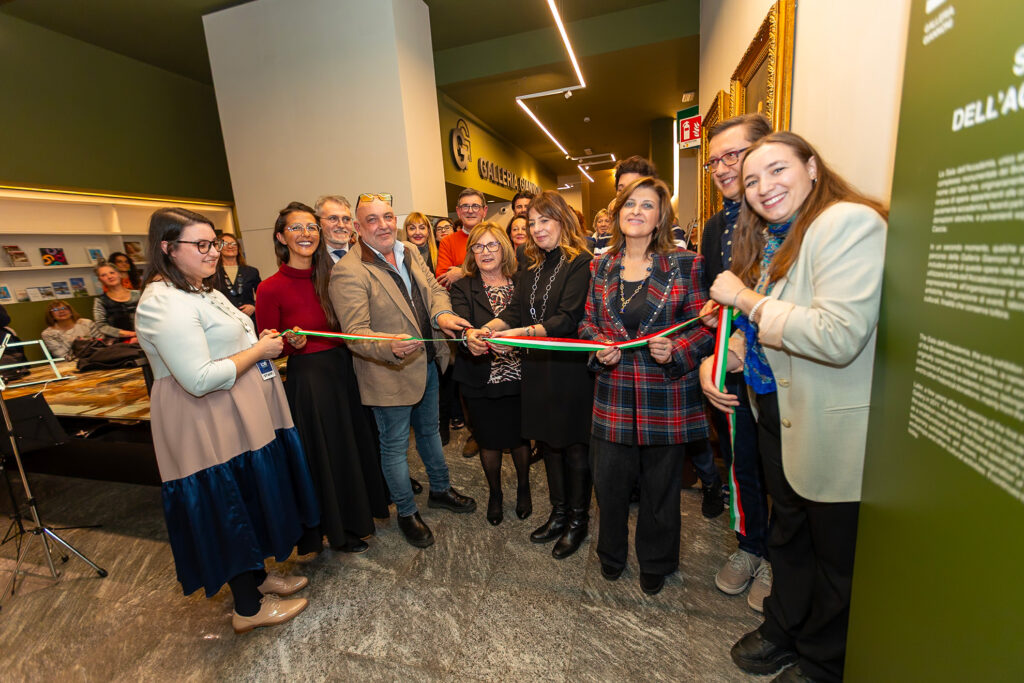 Gruppo di persone e rappresentanti istituzionali taglia il nastro tricolore durante l’inaugurazione della mostra a Novara