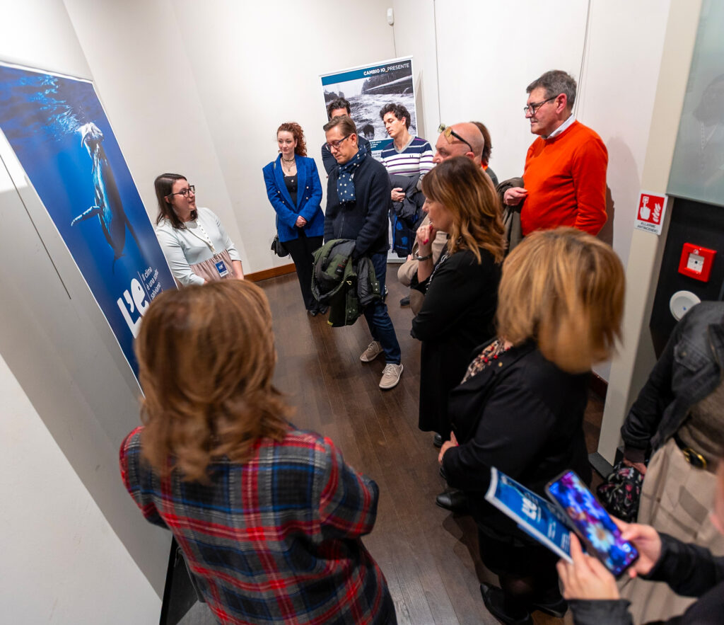 Una guida illustra i contenuti della mostra a un gruppo di persone raccolte davanti ai pannelli informativi.