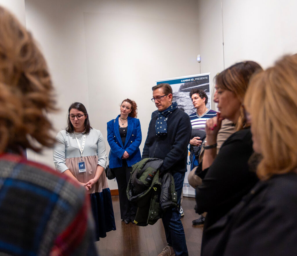 Parte del pubblico osserva un pannello informativo della mostra mentre ascolta la spiegazione.