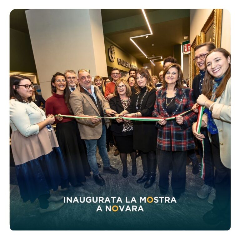 Taglio del nastro all’inaugurazione della mostra a Novara: un gruppo di persone e rappresentanti istituzionali tiene il nastro tricolore all’ingresso dello spazio espositivo.