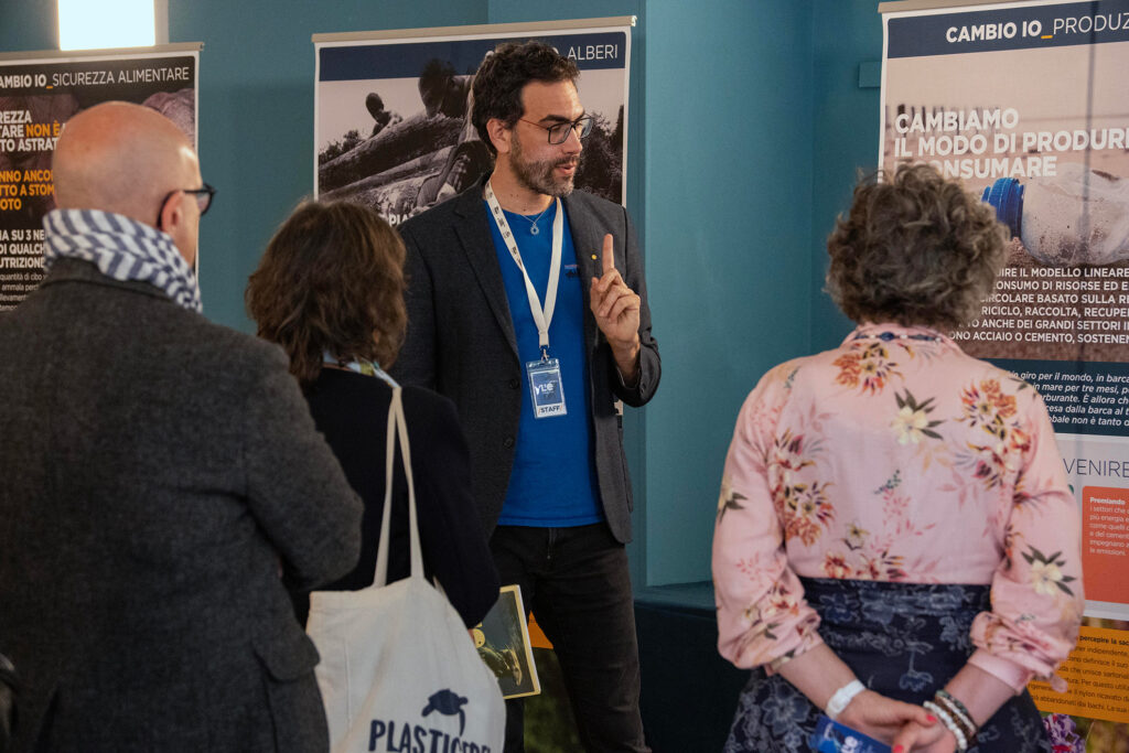 Persona con badge staff spiega un pannello della mostra a un piccolo gruppo di visitatrici e visitatori.