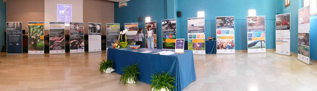 Sala espositiva con pannelli informativi disposti lungo le pareti e un tavolo centrale con materiali e decorazioni.