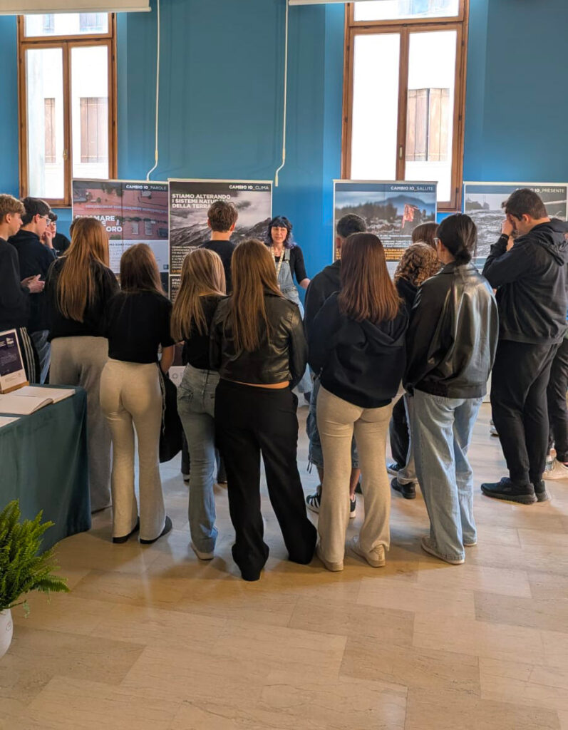 Gruppo di giovani ascolta una guida davanti ai pannelli della mostra dedicata alla crisi climatica.