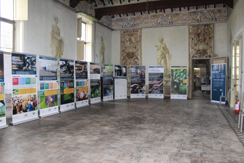 Pannelli della mostra “L’eredità della vita” esposti in una sala storica affrescata.